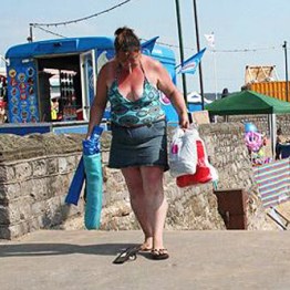 Fat , sunburned woman with cigarette and flip flops at the seaside